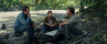 Movie still from “Jungle” (2017), directed by Greg McLean – A group of men sitting on a rocky ground; Medium shot, Over the shoulder angle