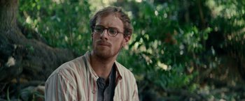 Movie still from “Jungle” (2017), directed by Greg McLean – A person wearing glasses with trees in the background; Close Up shot, Over the shoulder angle