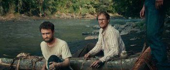 Movie still from “Jungle” (2017), directed by Greg McLean – Two men sitting next to each other on a log; Medium shot, High angle