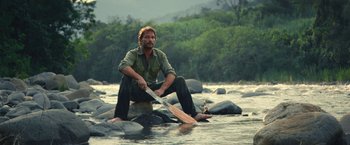 Movie still from “Jungle” (2017), directed by Greg McLean – A man kneeling down in a river holding a knife; Wide shot, Low angle
