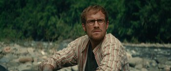 Movie still from “Jungle” (2017), directed by Greg McLean – A person wearing glasses with trees in the background; Close Up shot, Over the shoulder angle