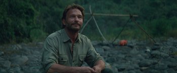 Movie still from “Jungle” (2017), directed by Greg McLean – A person sitting on the ground near rocks; Close Up shot, Over the shoulder angle