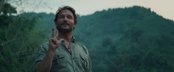 Movie still from “Jungle” (2017), directed by Greg McLean – A man in a green shirt is giving the peace sign; Close Up shot, Over the shoulder angle