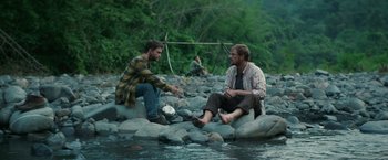 Movie still from “Jungle” (2017), directed by Greg McLean – Two men sitting on rocks in the water; Wide shot, Over the shoulder angle