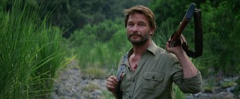 Movie still from “Jungle” (2017), directed by Greg McLean – A man with a beard is standing in the grass; Close Up shot, Over the shoulder angle