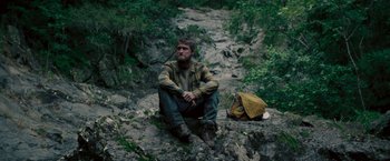 Movie still from “Jungle” (2017), directed by Greg McLean – A man sitting on the ground near a backpack; Medium shot, High angle