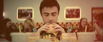 Movie still from “Jungle” (2017), directed by Greg McLean – A man sitting at a table eating a hamburger and french fries; Close Up shot, Overhead angle