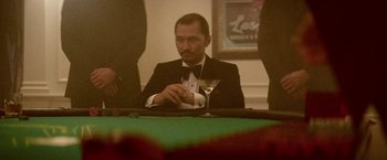 Movie still from “Jungle” (2017), directed by Greg McLean – A man sitting at a table with a drink in front of him; Medium shot, Over the shoulder angle