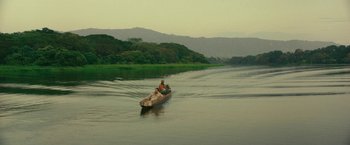 Movie still from “Jungle” (2017), directed by Greg McLean – A man in a boat on a river with trees in the background; Extreme Wide shot, High angle