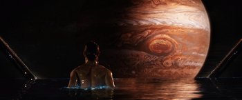 Movie still from “Jupiter Ascending” (2015), directed by Lilly Wachowski – A man sitting in a body of water looking at the sky; Extreme Wide shot, High angle
