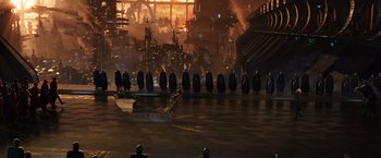Movie still from “Jupiter Ascending” (2015), directed by Lilly Wachowski – A group of people standing on a stage in front of a building; Extreme Wide shot, High angle