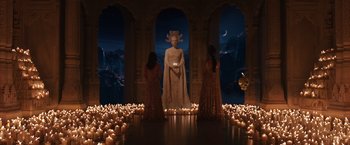 Movie still from “Jupiter Ascending” (2015), directed by Lilly Wachowski – Three women standing in front of a statue of a woman in front of candles; Extreme Wide shot, Over the shoulder angle