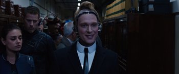 Movie still from “Jupiter Ascending” (2015), directed by Lilly Wachowski – A man in a suit and tie wearing headphones; Close Up shot, High angle
