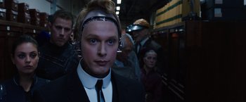 Movie still from “Jupiter Ascending” (2015), directed by Lilly Wachowski – A man in a suit and tie wearing a head piece; Close Up shot, Over the shoulder angle