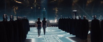 Movie still from “Jupiter Ascending” (2015), directed by Lilly Wachowski – Two people walking on a stage in front of a man; Wide shot, Over the shoulder angle