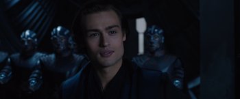 Movie still from “Jupiter Ascending” (2015), directed by Lilly Wachowski – A man in a black robe and some blue statues; Close Up shot, Over the shoulder angle