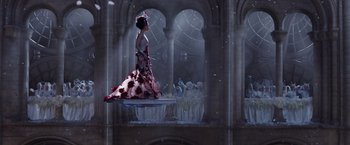 Movie still from “Jupiter Ascending” (2015), directed by Lilly Wachowski – A woman in a red and white dress standing in front of a group of people; Wide shot, Low angle