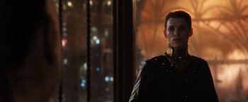 Movie still from “Jupiter Ascending” (2015), directed by Lilly Wachowski – A man wearing a black leather jacket and a gold collar standing in front of a window; Close Up shot, Over the shoulder angle