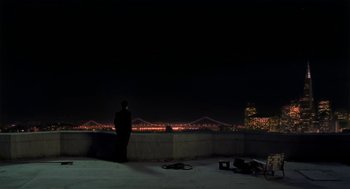 A man standing on a balcony at night looking out at a bridge