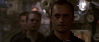Movie still from “K-19: The Widowmaker” (2002), directed by Kathryn Bigelow – A man in a black shirt is looking at the camera; Close Up shot, Over the shoulder angle
