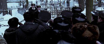 Movie still from “K-19: The Widowmaker” (2002), directed by Kathryn Bigelow – A group of people wearing hats in front of an image of an oil field; Wide shot, Over the shoulder angle