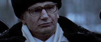 Movie still from “K-19: The Widowmaker” (2002), directed by Kathryn Bigelow – An older man wearing glasses and a hat; Close Up shot, Over the shoulder angle
