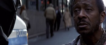 Movie still from “K-PAX” (2001), created by Robert Cochran – A man standing on a sidewalk with people walking in the background; Close Up shot, Over the shoulder angle