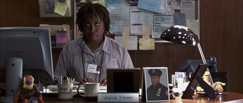 Movie still from “K-PAX” (2001), created by Robert Cochran – A woman sitting at a desk in front of a picture of a police officer; Medium shot, High angle