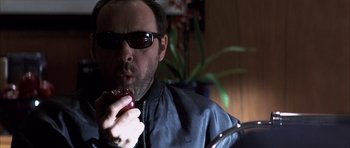 Movie still from “K-PAX” (2001), created by Robert Cochran – A man wearing sunglasses eating a donut; Close Up shot, Low angle