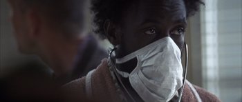 Movie still from “K-PAX” (2001), created by Robert Cochran – A person wearing a face mask and a pink sweater; Close Up shot, Low angle