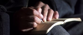 Movie still from “K-PAX” (2001), created by Robert Cochran – A person is writing in a notebook with a pen; Extreme Close Up shot, High angle