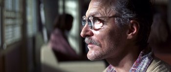 Movie still from “K-PAX” (2001), created by Robert Cochran – An older man wearing glasses looking into the distance; Close Up shot, Low angle