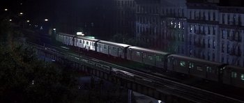 Movie still from “K-PAX” (2001), created by Robert Cochran – A train traveling down tracks next to a bridge at night; Extreme Wide shot, High angle