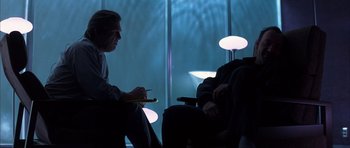 Movie still from “K-PAX” (2001), created by Robert Cochran – Two people are sitting in a dark room; Medium shot, Over the shoulder angle