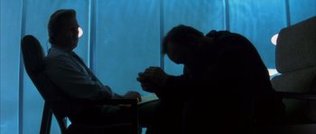 Movie still from “K-PAX” (2001), created by Robert Cochran – A man sitting in front of a window with his head down; Medium shot, Low angle