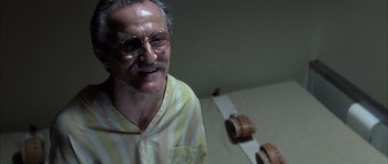 Movie still from “K-PAX” (2001), created by Robert Cochran – An older man wearing glasses and a yellow and white striped shirt; Close Up shot, Low angle