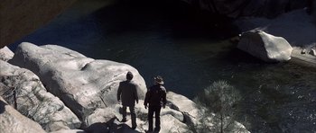 Movie still from “K-PAX” (2001), created by Robert Cochran – Two people standing on a cliff looking down at the water; Extreme Wide shot, Overhead angle