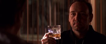 Movie still from “K-PAX” (2001), created by Robert Cochran – A man is holding a glass of whiskey; Close Up shot, Overhead angle