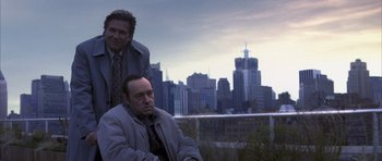 Movie still from “K-PAX” (2001), created by Robert Cochran – Two men sitting in front of a city skyline; Medium shot, Low angle