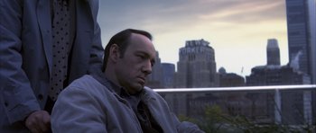 Movie still from “K-PAX” (2001), created by Robert Cochran – A man sitting on top of a building in front of a city skyline; Close Up shot, Low angle