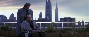 Movie still from “K-PAX” (2001), created by Robert Cochran – A man sitting on a bench next to another man; Wide shot, Low angle