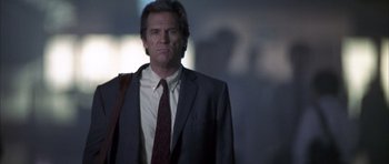 Movie still from “K-PAX” (2001), created by Robert Cochran – A man wearing a suit and tie standing in a dark room; Medium shot, Low angle