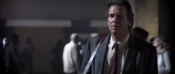 Movie still from “K-PAX” (2001), created by Robert Cochran – A man in a suit and tie standing in front of a crowd; Close Up shot, Low angle