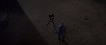 Movie still from “K-PAX” (2001), created by Robert Cochran – A man standing next to a camera on top of a tripod; Extreme Wide shot, Overhead angle