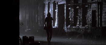 Movie still from “Kalifornia” (1993), directed by Dominic Sena – A woman walking in the rain holding a bag; Wide shot, Low angle