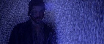 Movie still from “Kalifornia” (1993), directed by Dominic Sena – A man standing in the middle of a rain storm; Medium shot, Low angle