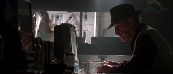 Movie still from “Kalifornia” (1993), directed by Dominic Sena – A man sitting in front of a computer on top of a desk; Medium shot, Low angle