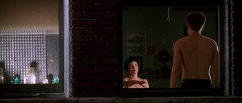 Movie still from “Kalifornia” (1993), directed by Dominic Sena – A woman looking in a mirror in a dark room; Medium shot, Over the shoulder angle