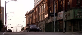 Movie still from “Kalifornia” (1993), directed by Dominic Sena – A car parked on the side of the road in front of some buildings; Extreme Wide shot, Low angle