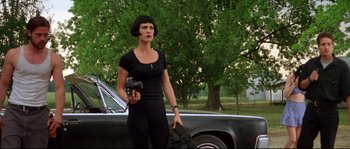 Movie still from “Kalifornia” (1993), directed by Dominic Sena – A woman holding a camera standing in front of a car; Medium shot, Low angle